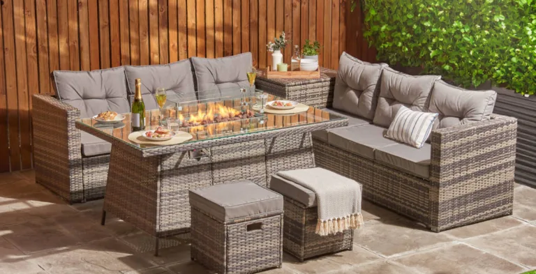A display of stylish garden furniture, showing grey rattan chairs, a dining table and a fire pit.